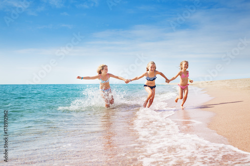 Girls running in sand and waves of sunny beach