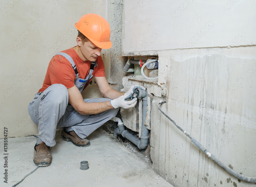 Worker is putting a gypsum plaster on a wall. He is using a long rule.