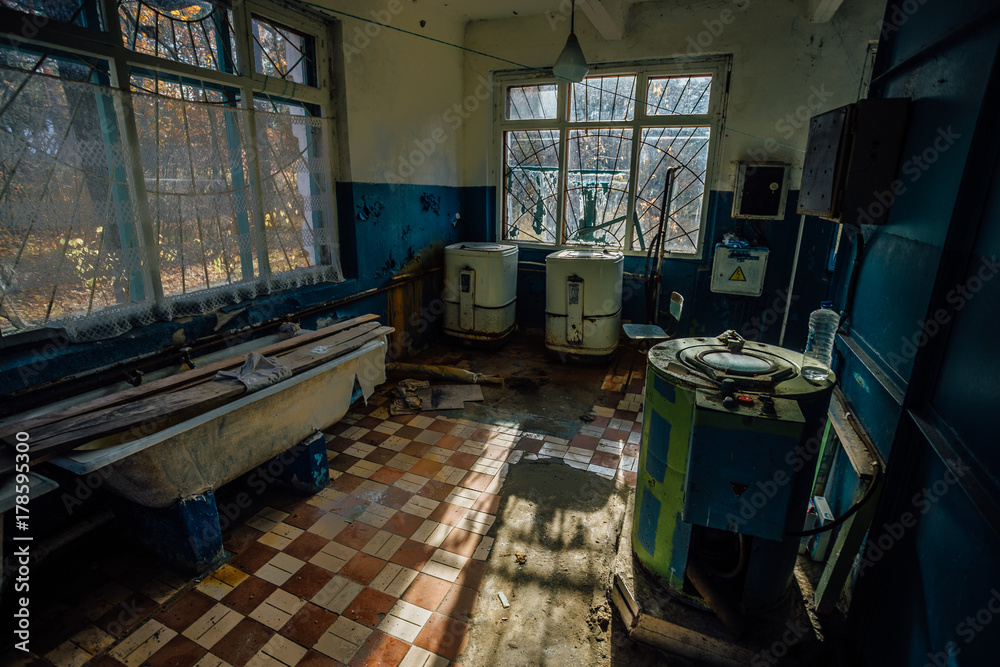 Sinister and creepy old laundry room with a dirty floor and broken wash machines and bathes in an abandoned psychiatric hospital. Sinister and creepy old laundry room with a dirty floor and broken wash machines and bathes in an abandoned psychiatric hospital.