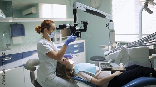 Female dentist with dental tools - microscope, mirror and probe treating patient teeth at dental clinic office. Medicine, dentistry and health care concept. Dental equipment