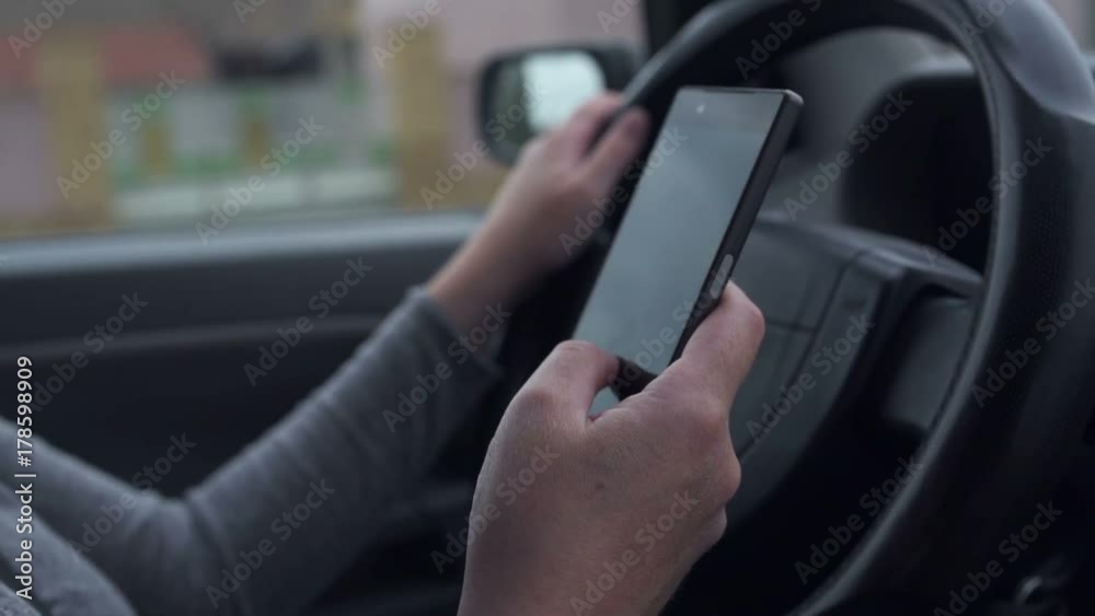 Woman driving and texting on mobile smartphone while holding the steering wheel