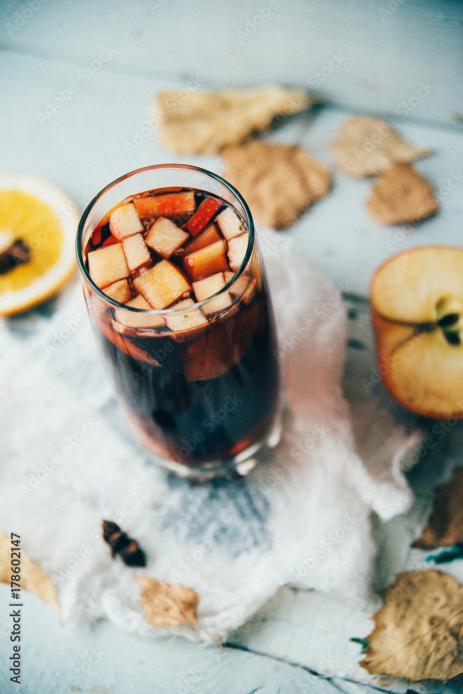 Fototapeta premium Hot mulled wine in a glass with orange slices, anise and cinnamon sticks, star cookies on vintage wood table. Christmas or winter warming drink with recipe ingredients around