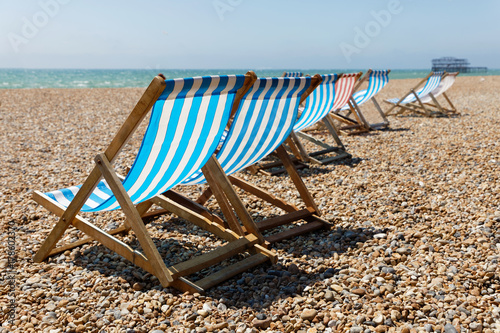 Classic blue, red and white striped empty deckchairs on the beach. The old pier in Brighton in the background © hans_chr