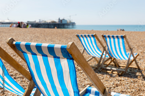 Classic blue striped empty deckchairs on the beach. The new pier in Brighton and people in the background
