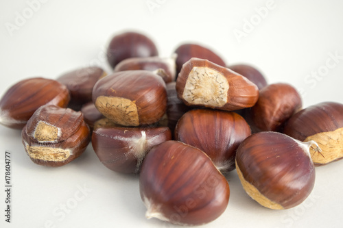 Raw sweet chestnuts scattered on a white background, tasty and healthy brownish nuts