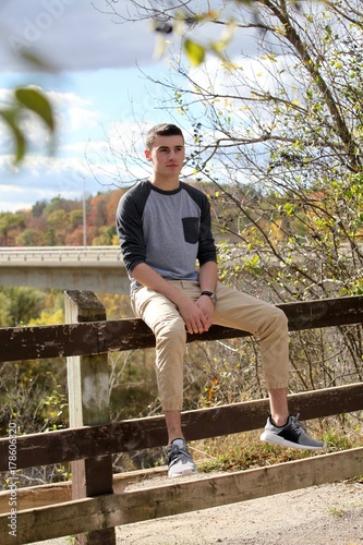 Teenage boy sitting on a fence looking into the distance and pondering