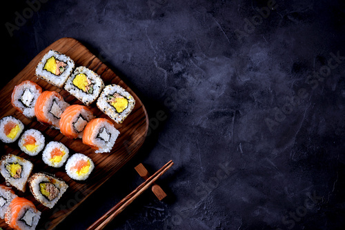 Sushi with wasabi and marinated ginger on an olive board on a black concrete background.