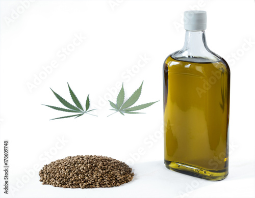 Hemp oil in a bottle with a bunch of marijuana seeds and a marijuana leaf. Isolated on white background.