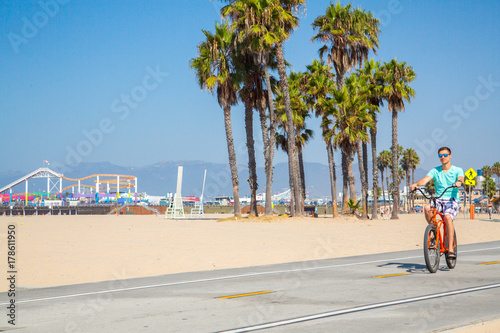 Young man riding a beach bike down the Venice beach in Los Angeles near Santa Monica pier.