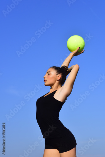 Woman gymnast in black sportswear with green ball.