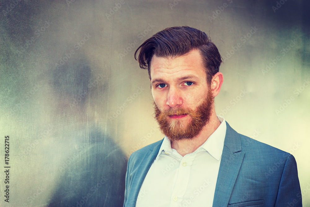 Portrait of American Business in New York. Wearing cadet blue suit, white undershirt, a college graduate student with beard, mustache standing by silver metal wall, looking at you. Instagram effect..