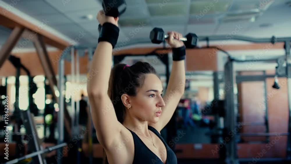 Young sports woman brunette with long hair doing exercises with dumbbells in the gym. 4 k Young sports woman brunette with long hair doing exercises with dumbbells in the gym. 4 k