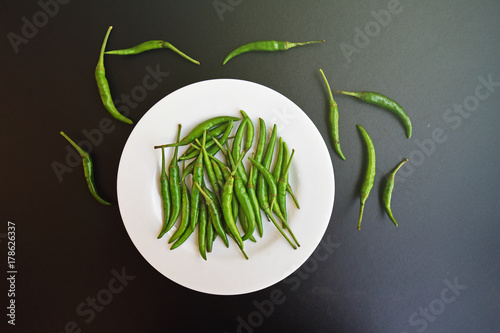 Green chilli on in white plate on dark kitchen table background.