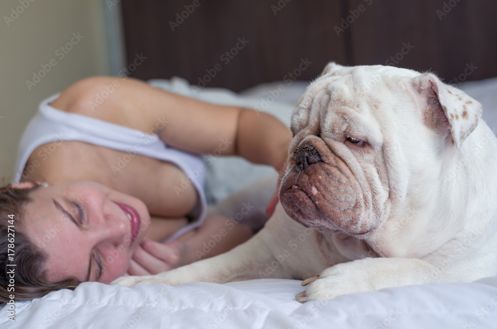 Jovem mulher loira brincando com pet, cachorro, bulldog inglês na cama. Companheiro pet