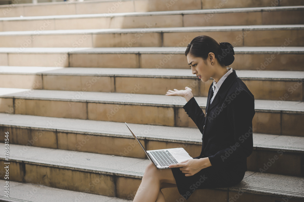 Young woman sitting on staircase using laptop computer. Female working on laptop in an outdoor