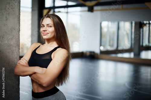 Portrait of beautiful fitness coach woman with long hair and a smile in gym space. Hard work and dedication is the path to perfect body. Healthy life concept.