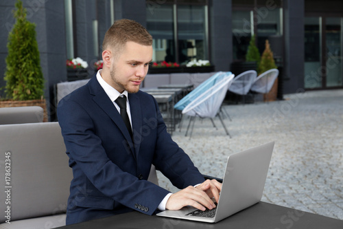 Handsome man in suit sitting with his laptop outdoors