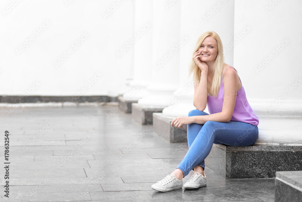 Beautiful young woman sitting near column outdoors