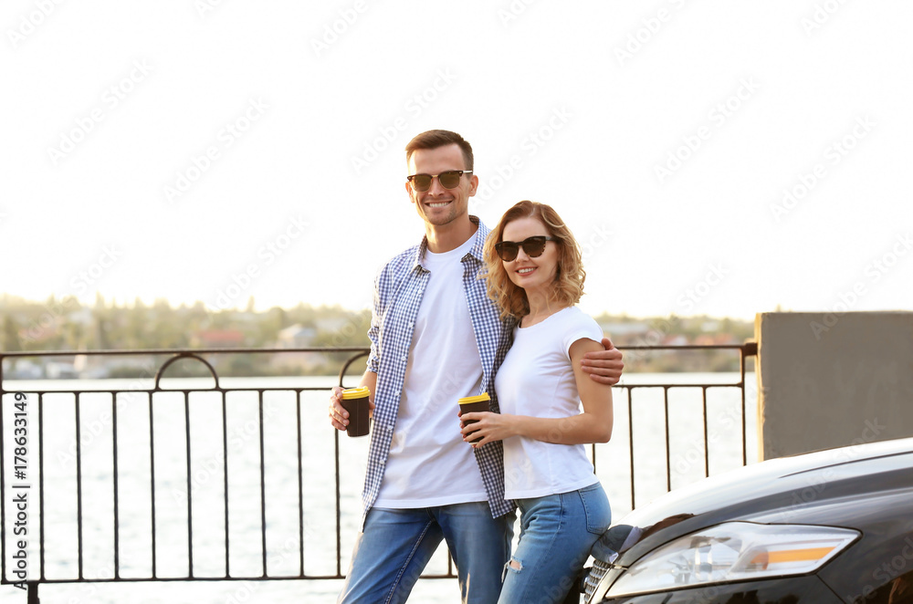 Beautiful young couple with coffee standing near car Beautiful young couple with coffee standing near car