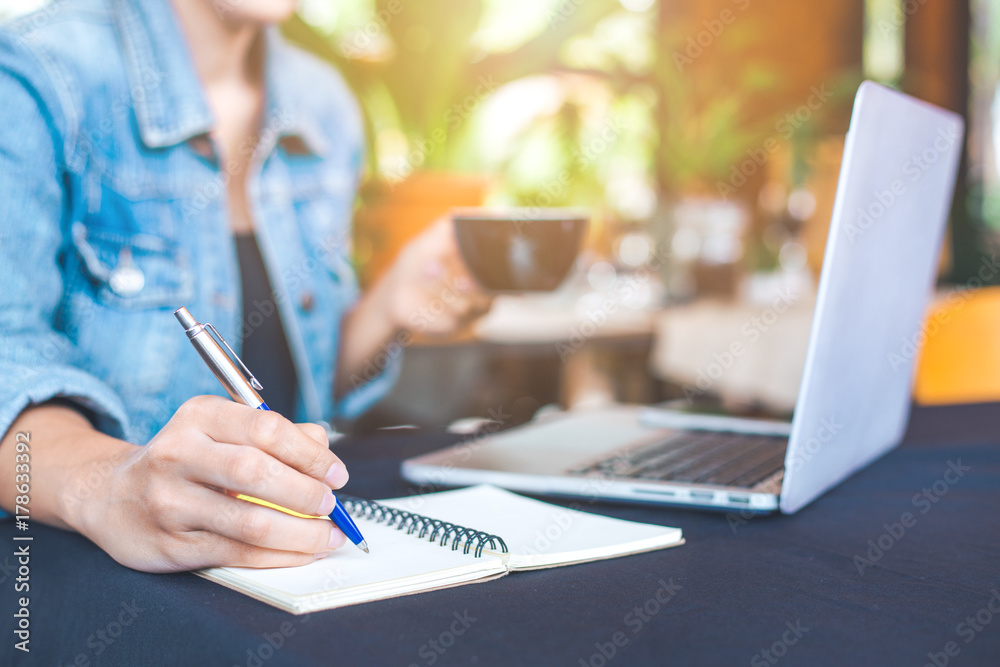 Woman hand works in a laptop computer and is writing on notepad with a pen in the office. Woman hand works in a laptop computer and is writing on notepad with a pen in the office.