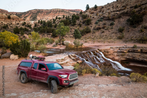 Red pickup camping rig on rocky trail near waterfall in southern Utah photo