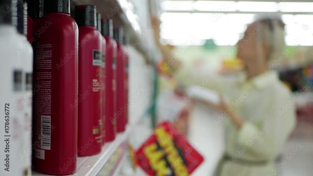 Blurred young woman choosing hair conditioner or shampoo in a beauty shop. Woman holding a body care product Blurred young woman choosing hair conditioner or shampoo in a beauty shop. Woman holding a body care product