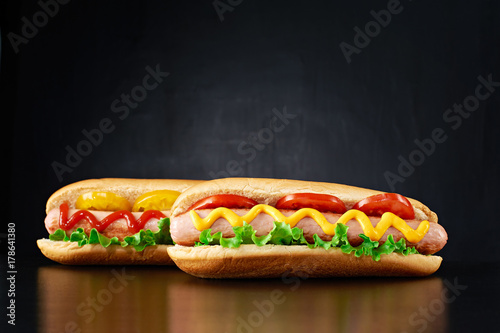Two big hotdog with sausage tomatoes, mustard, ketchup and salad isolated on black background. Front view.