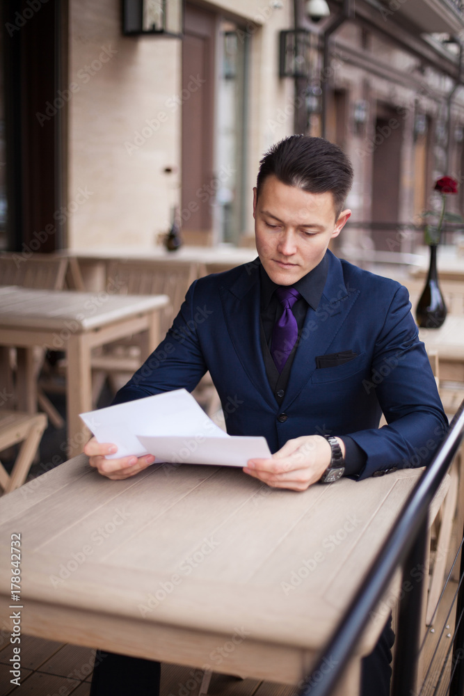 A young man in a blue business suit, a lunch break in a cafe, carefully reading the documents.