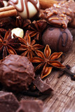 A selection of assorted chocolate truffle pralines on a wooden table with dark chocolate, cinnamon and anise.