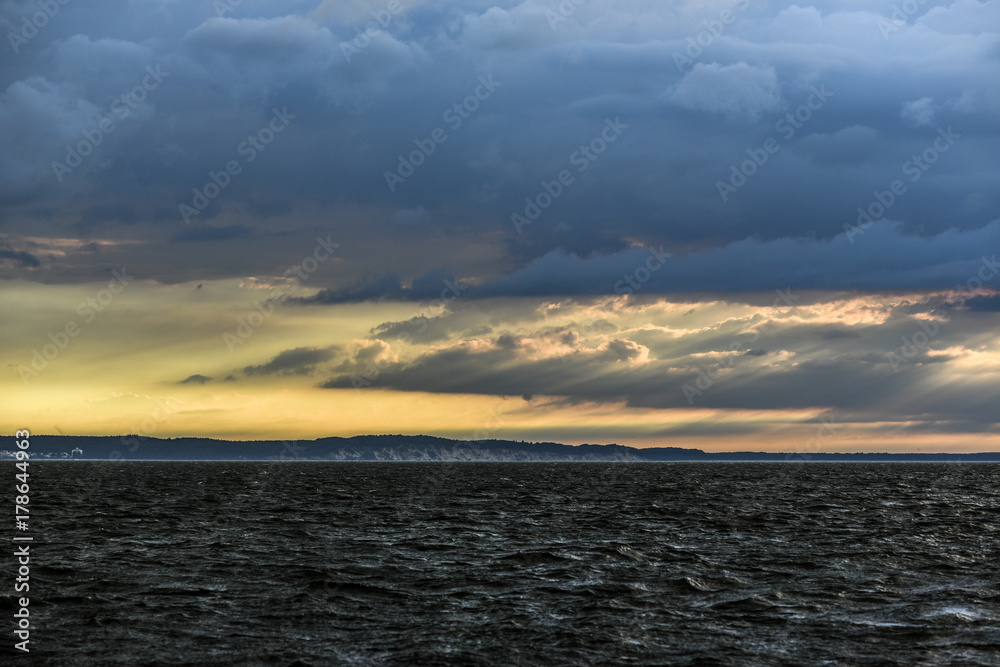 German coast with clouds and yellow sun on the horizon in the Baltic Sea.