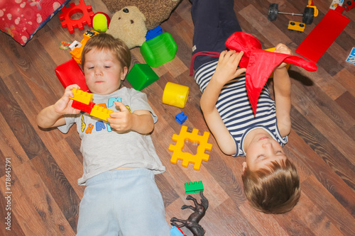 Children lie on the floor among the toys. The children made the mess and lay down on the floor..