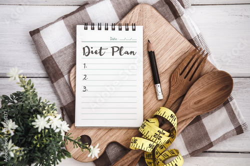 Line Notepad with Diet Plan list text  on chopping board with wooden fork and spoon and the  measuring tape on white table , recipes food or diet plan for healthy habits shot note background concept