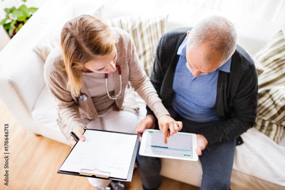 Health visitor and a senior man with tablet during home visit. - obrazy, fototapety, plakaty 