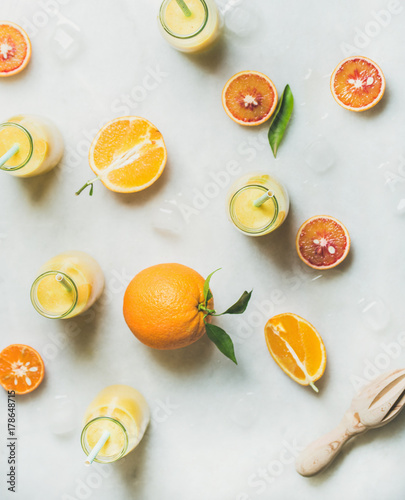 Healthy yellow smoothie with citrus fruit, ginger and ice in bottles over light marble table background, top view. Clean eating, vegan, vegetarian, detox, dieting, weight loss food concept