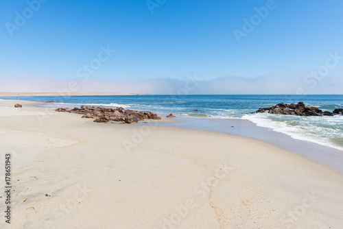 Sandy beach and coast line on the Atlantic ocean at Cape Cross, Namibia, famous for the nearby seal colony. Clear blue sky.