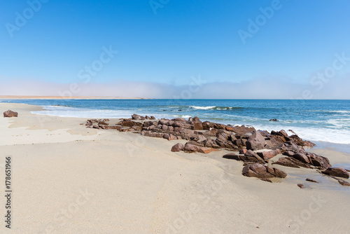 Sandy beach and coast line on the Atlantic ocean at Cape Cross, Namibia, famous for the nearby seal colony. Clear blue sky.