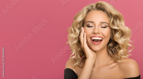 Blonde woman with curly beautiful hair smiling on pink background.