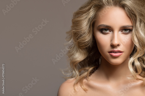 Blonde woman with curly beautiful hair on gray background.