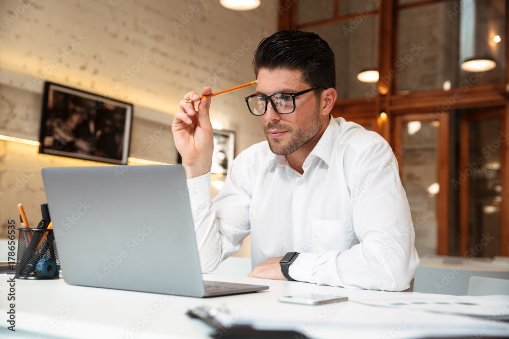 Φωτογραφία Close-up photo of thinking businessman in glasses holding pencil, looking at lap