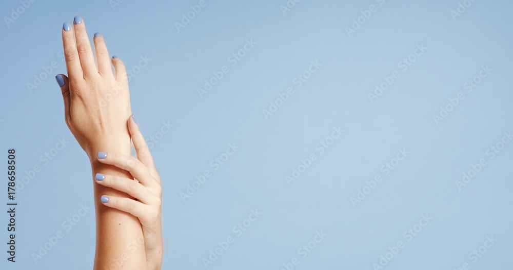 Clean well manicured hands of a young woman, applying hand cream, skin care on light blue background Clean well manicured hands of a young woman, applying hand cream, skin care on light blue background