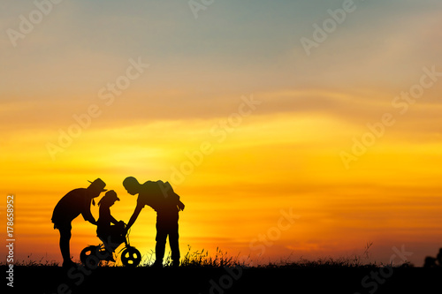 Warm family concept, silhouette of parents helping daughter to ride bicycle with funny and happy in sunset.