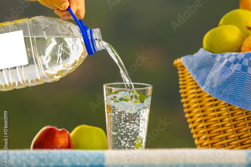 on a picnic in the open air pours into a glass of drinking water, near a basket of fruit, on a checkered blanket