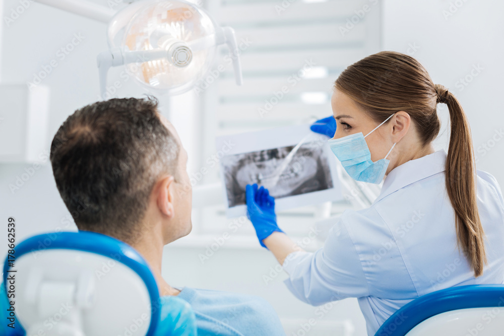 Nice joyful dentist pointing at the Xray photo Nice joyful dentist pointing at the Xray photo