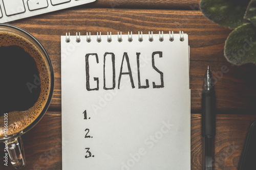 Top view of notepad with Goals List, cup of coffee on wooden table, goals concept photo