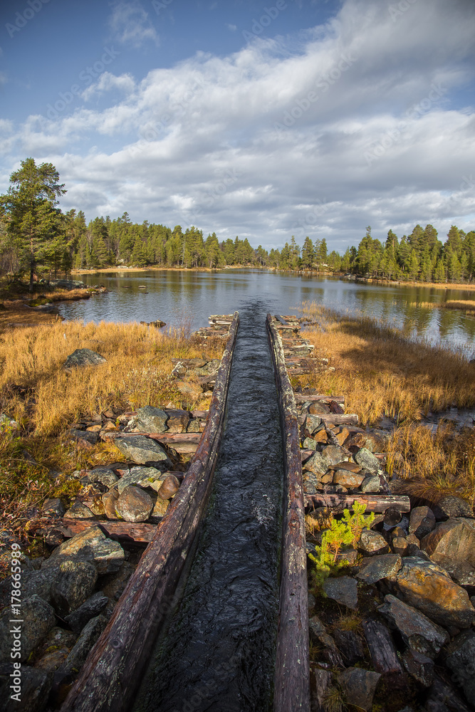 A beautiful autumn scenery of a historic water channel for transporting timber between lakes. Wooden construction.  Autumn in Femundsmarka National Park.