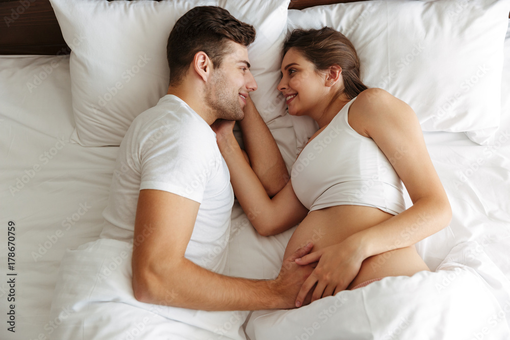 Cheerful pregnant woman lies in bed with husband Cheerful pregnant woman lies in bed with husband