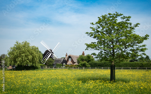 A traditional old English windmill and farm house cottage nestling in the spring English countryside. Cambridgeshire, UK.