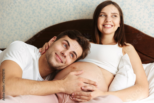 Happy young pregnant wife lying in bed with her husband