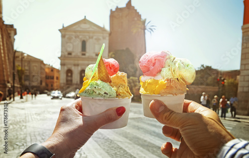 Couple with beautiful bright  sweet Italian ice-cream with different flavors  in the hands   on the square in Rome , Italy