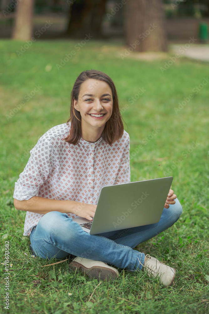Young woman with laptop sitting on green grass Young woman with laptop sitting on green grass